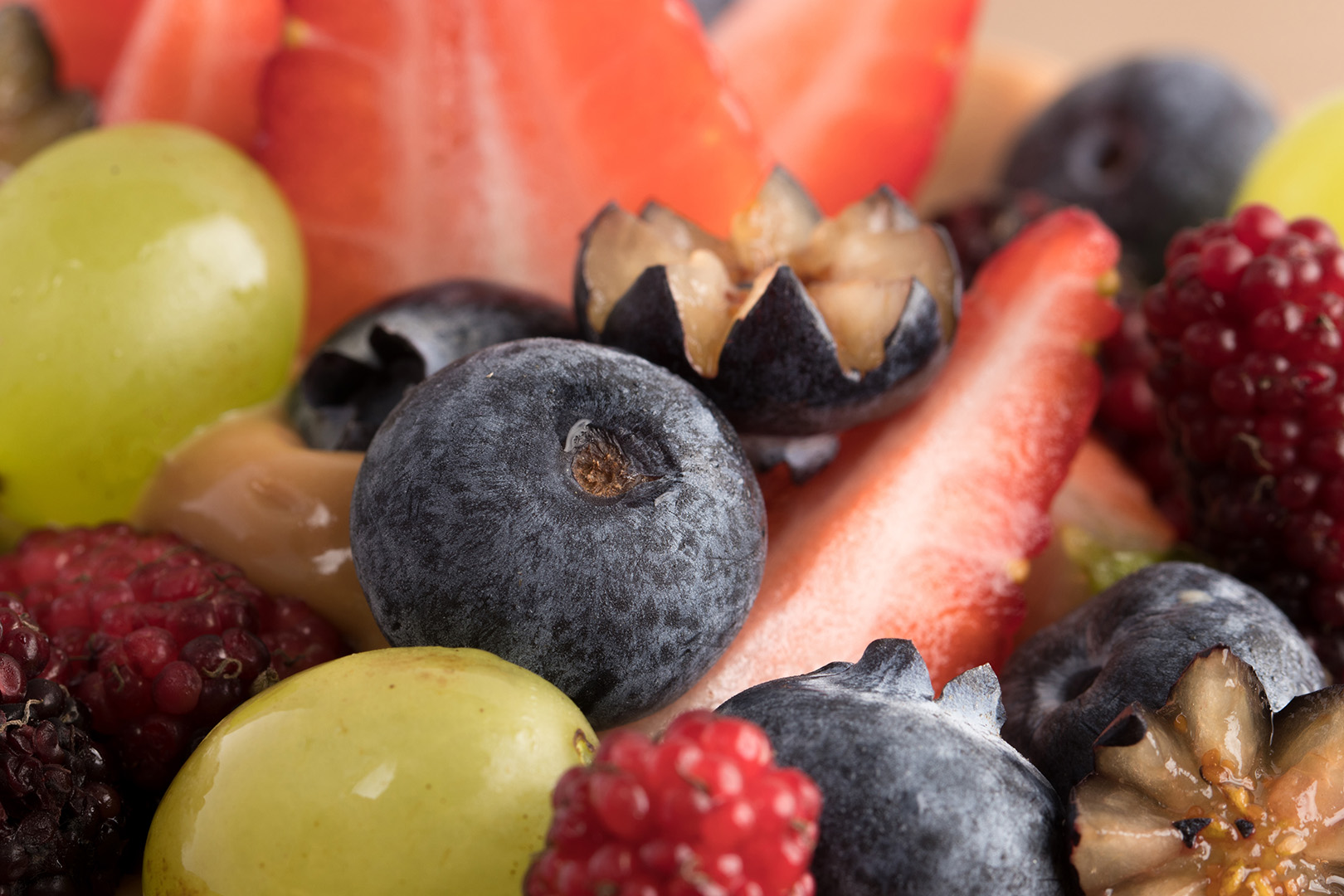 Imagem macro de frutas como martilho, morango, framboesa e uva no topo de um bolo de doce de leite