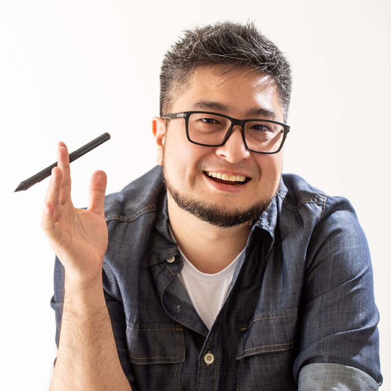 Foto do designer Denis Moribe sorrindo segurando uma caneta