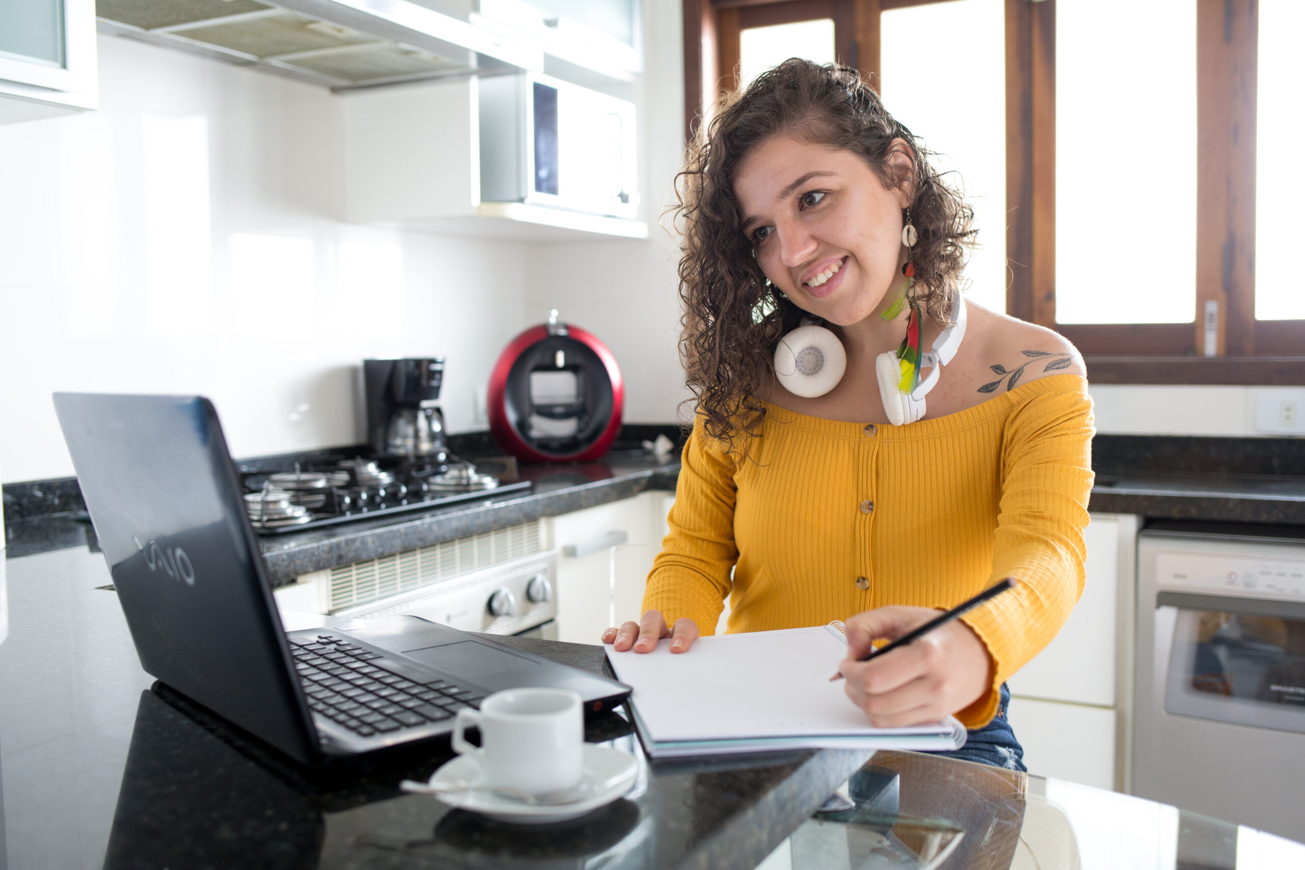 Imagem de uma mulher ouvindo música e tomando café em uma cozinha de manhã
